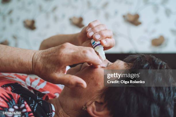 dry eye syndrome and eye drops. elderly woman applying eyedropper, home treatment for better eyesight - colírio imagens e fotografias de stock