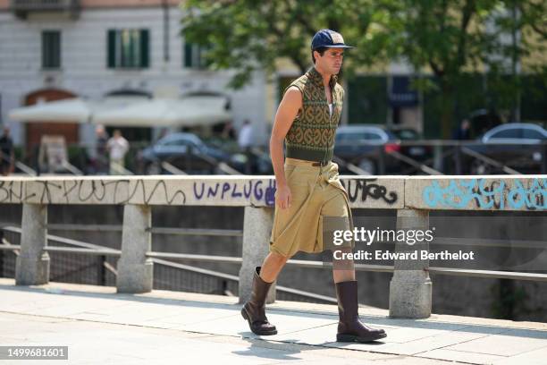 Guest wears a navy blue denim cap from Levis, silver earrings, a gold small chain necklace, a white tank-top, a green and orange embroidered print...