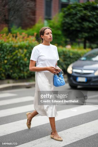Guest wears a white t-shirt, a royal blue shiny leather puffy pockets handbag from Prada, white latte silk satin midi skirt, beige suede ballerinas ,...