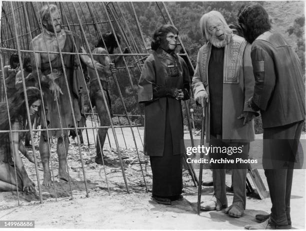 Charlton Heston tries to draw attention to his message written in the sand to Kim Hunter, Maurice Evans, and Roddy McDowall, who stand outside the...