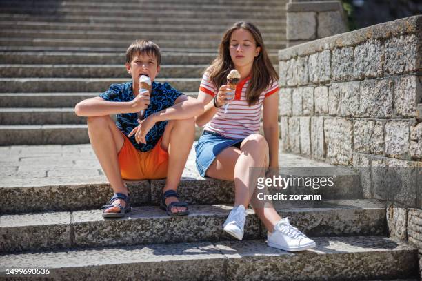 junge und seine schwester im teenageralter sitzen im sommer auf einer steintreppe und essen eis - croatia girls stock-fotos und bilder