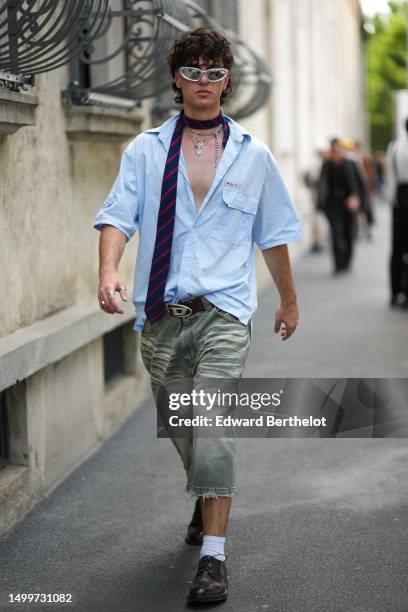 Guest wears silver sunglasses, a navy blue with burgundy striped print pattern silk tie, silver large chain long necklaces, a pale blue short sleeves...