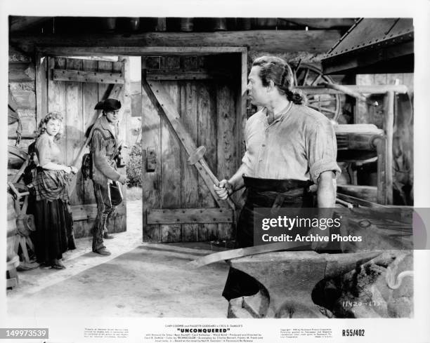 Paulette Goddard and Gary Cooper looking at man hammering metal as they walk out in a scene from the film 'Unconquered', 1947.