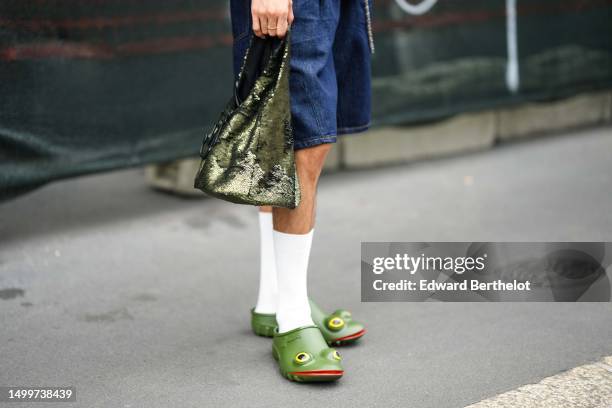 Guest wears blue denim shorts, a green sequined handbag, white socks, green plastic with yellow eyes and red lips mules in shape of frog , outside JW...