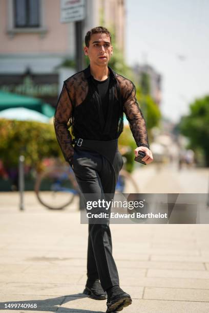 Guest wears a black halter neck tank-top, a black tulle with embroidered pattern long sleeves t-shirt, black suit pants, black ankle shoes , outside...