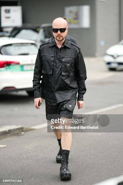 Guest wears black sunglasses, a black nylon cargo shirt from Prada, matching black cargo nylon shorts from Prada, black shiny leather laces ankle...