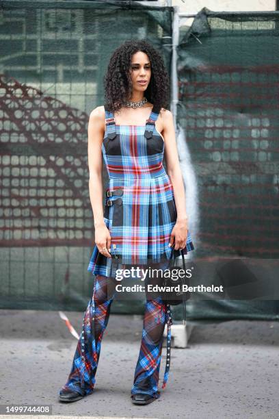 Guest wears a silver large chain necklace, a black with blue and red checkered print pattern tank-top / pleated / accordion short dress, matching...