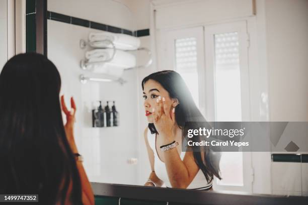 young woman applies make up in front of the bathroom mirror - vanity lights stock pictures, royalty-free photos & images