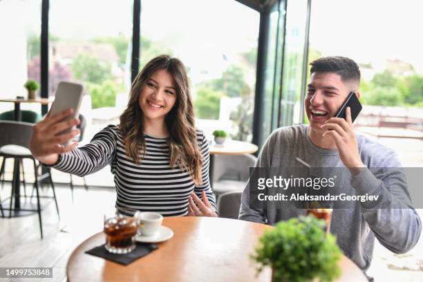lächelnde frau macht kaffee-selfie mit freund, während er telefoniert - dosen schießen stock-fotos und bilder