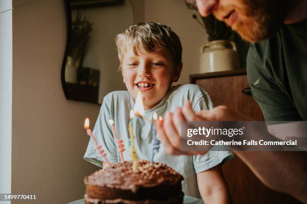 a father lights the birthday candles on his son's birthday cake - milestone stock-fotos und bilder