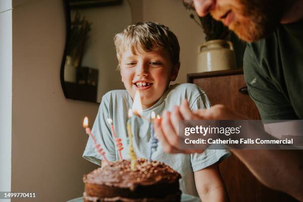 a father lights the birthday candles on his son's birthday cake - moment friends men european stockfoto's en -beelden