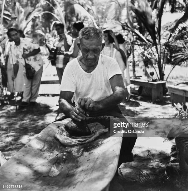 Man preparing Poi, a traditional Hawaiian vegetable dish, mashing cooked starch using a carved pestle on a wooden pounding board, Hawaii, circa 1955.