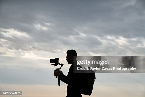 Camera Operator Silhouette At Work Using Stabilizer Against Sky Camera Operator Silhouette At Work Using Stabilizer Against Sky