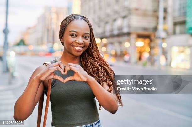 portrait of beautiful young woman making heart shape with hands in city - hand sign stock pictures, royalty-free photos & images