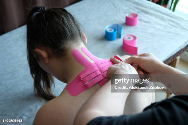 a young woman is lying on a table in a rehabilitation clinic, in the office of a doctor, masseur, rehabilitologist, physiotherapist. a physiotherapy specialist applies kinesio tape to the back, neck, spine. an osteopath does taping. alternative treatment. - elastic bandage 個照片及圖片檔