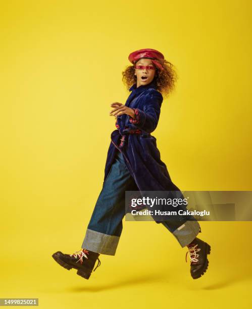 little girl looking at camera while jumping in front of yellow background. - jumping casual clothing studio shot stock pictures, royalty-free photos & images