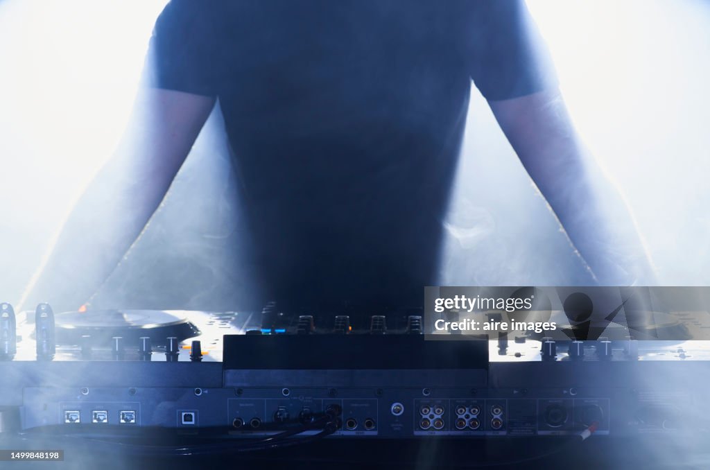 Front silhouette of a dj in casual clothes standing at the console turned on with light effects.