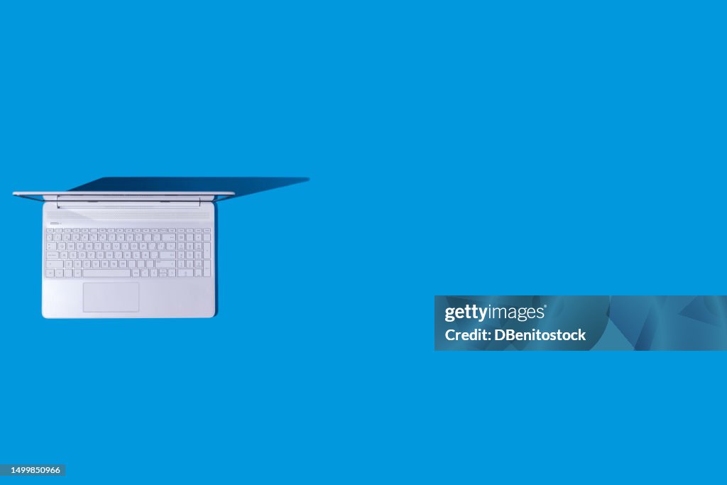 White laptop with hard shadow, on the left side, on blue background. Computer, Internet, PC, laptop and telecommuting concept.