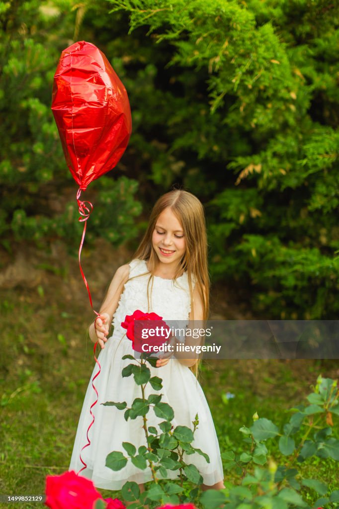 Blonde girl in white dress with red balloon. Summer lifestyle. Childhood