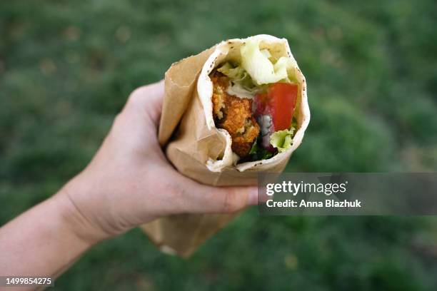 falafel wrap in female hand held oudoors. vegan street food concept. - cucina del medio oriente foto e immagini stock
