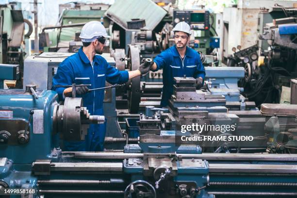 2 young engineers are workers and engineers in the factory helping to produce and form steel by working with the factory machines, including lathes and rolling machines. - operaio metallurgico foto e immagini stock