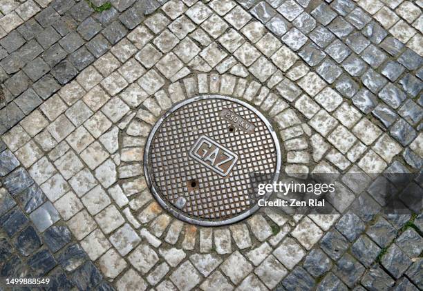 circular cast iron gas hole cover on black and white stone pavement - マンホール ストックフォトと画像