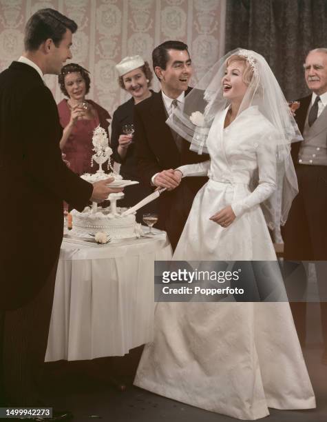 Posed portrait of a wedding scene with the bride, dressed in a traditional white wedding gown and veil, and groom surrounded by guests as the happy...