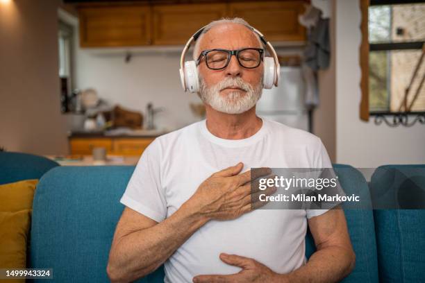 a mature senior man sits on a bed and practices guided meditation in his home - self discipline imagens e fotografias de stock