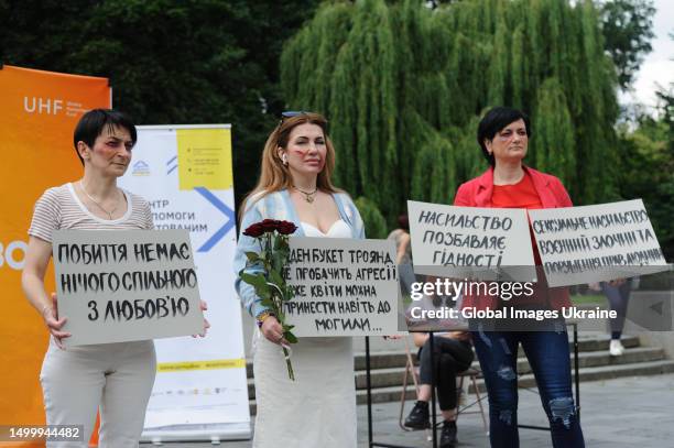 Women with make-up on their faces in the form of cuts and bruises typical of victims of domestic or sexual violence hold placards with the...