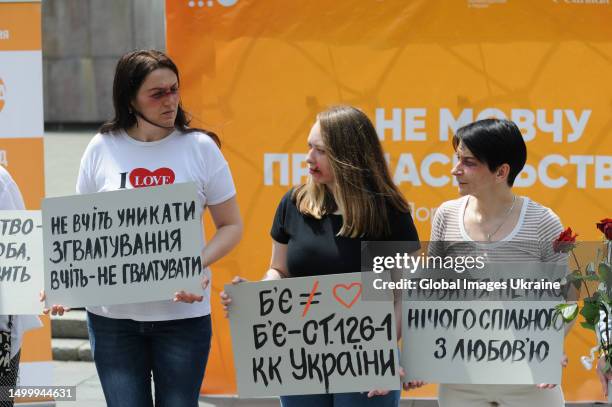 Women with make-up on their faces in the form of cuts and bruises typical of victims of domestic or sexual violence hold placards with the...