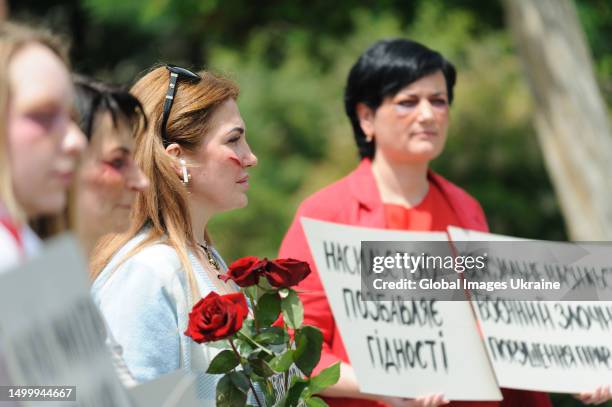 Women with make-up on their faces in the form of cuts and bruises typical of victims of domestic or sexual violence hold placards with the...