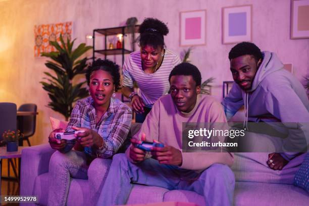 group of friends having fun playing video games at home at night - adrenaline junkie stock pictures, royalty-free photos & images