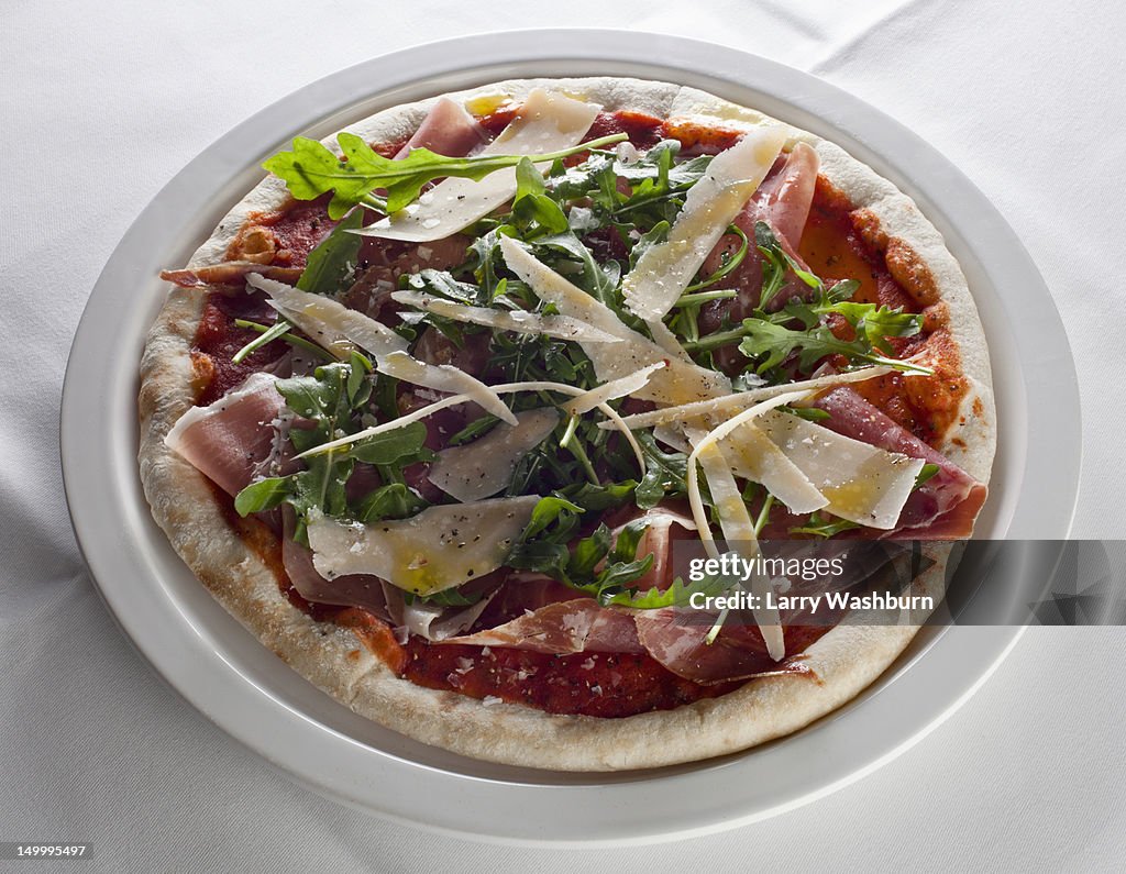 A pizza with ham, rocket, and cheese