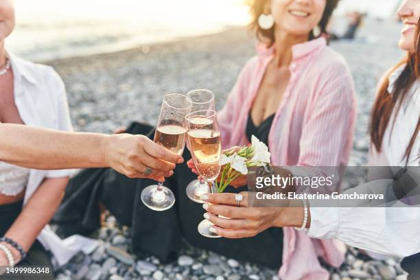 close-up shot of friends clinking sparkling wine glasses at sunset on the beach - asian female friends drinking soda outdoor stockfoto's en -beelden