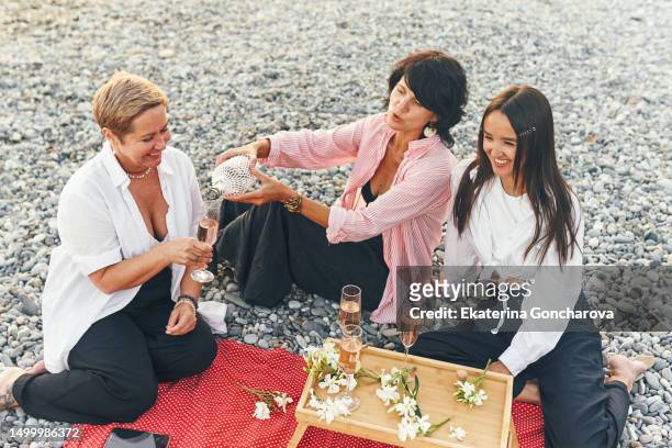 a friend pours champagne into glasses at a picnic by the sea - asian female friends drinking soda outdoor stockfoto's en -beelden