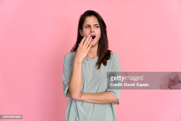 young girl in pajamas yawning on a pink background - yawning stockfoto's en -beelden