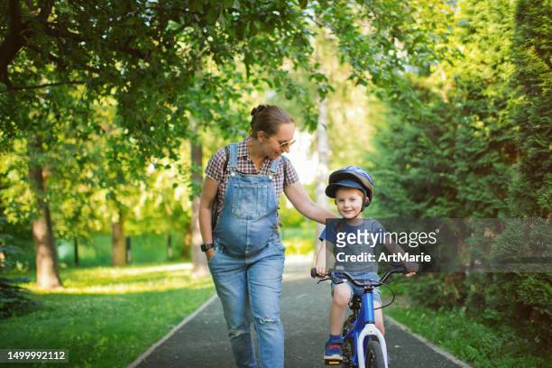 pregnant woman and her little boy riding a bicycle in summer - pregnancy class stockfoto's en -beelden