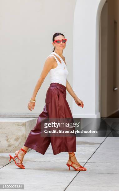 Influencer Anna von Schilcher, wearing bordeaux colored wide cutted 3/4 long leather pants by Marni, a white ribbed top by Remain, red sandals by the...
