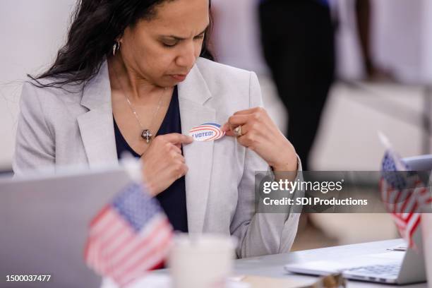 mid adult woman strategically places her "i voted" sticker on her jacket for all to see - vote sticker stock pictures, royalty-free photos & images