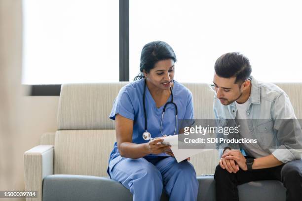 young man and female doctor review the medical chart together - man talking to doctor stock pictures, royalty-free photos & images
