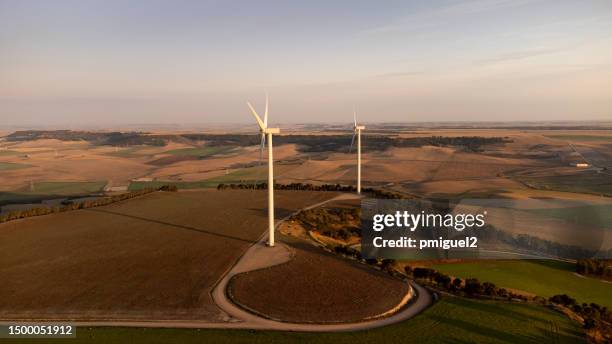 wind turbines on the top of a hill surrounded by farmland - recursos sostenibles stockfoto's en -beelden