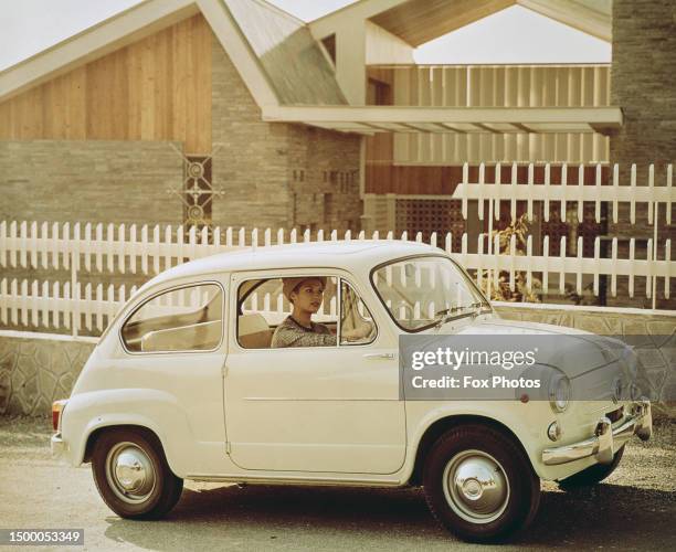 Publicity shot of a woman driving a Fiat 500 motorcar outside a modernist building, circa 1960.