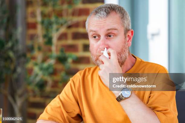man suffering from hay fever allergy using nasal spray - slijm stockfoto's en -beelden
