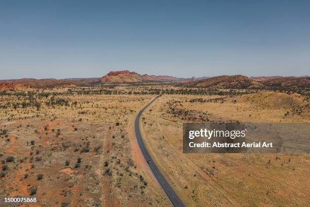 aerial shot showing a vehicle driving towards a mountainous area on a remote asphalt road during a sunny day, northern territory, australia - driving car australia road copy space sunlight travel destinations colour image day getting stock pictures, royalty-free photos & images