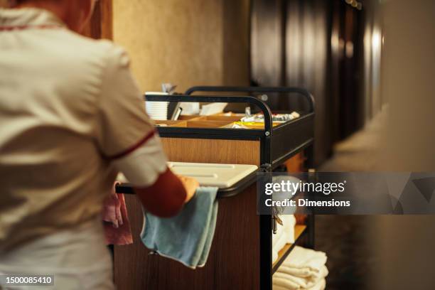 maid pushing sanitary trolley down hotel hallway - maid stock pictures, royalty-free photos & images