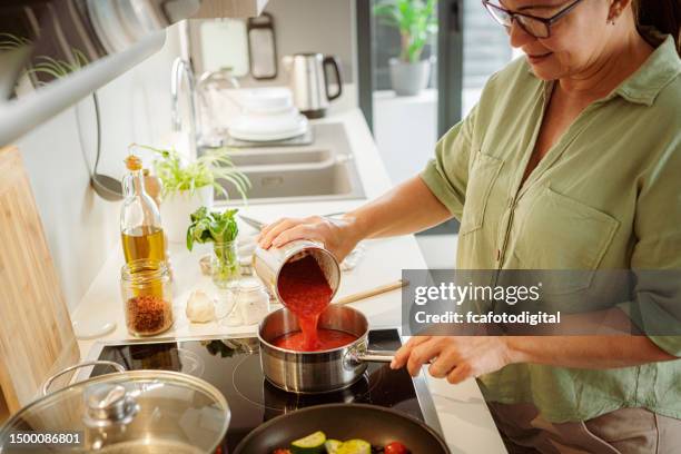 woman in kitchen preparing tomato sauce - tin stock pictures, royalty-free photos & images