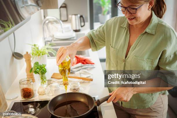 happy woman pouring cooking oil to a frying pan - house warm heating oil stockfoto's en -beelden