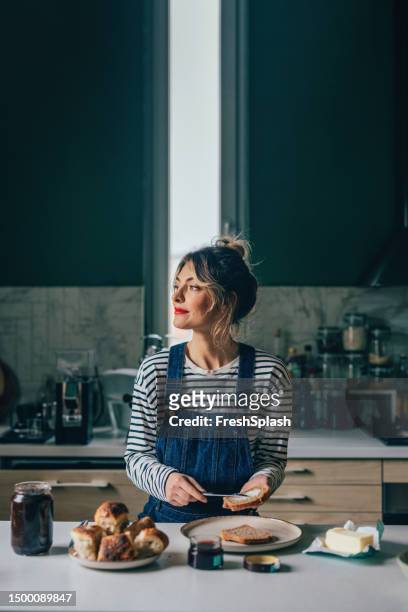 a happy beautiful blonde woman looking away while having breakfast at home in the morning - eating bread stockfoto's en -beelden