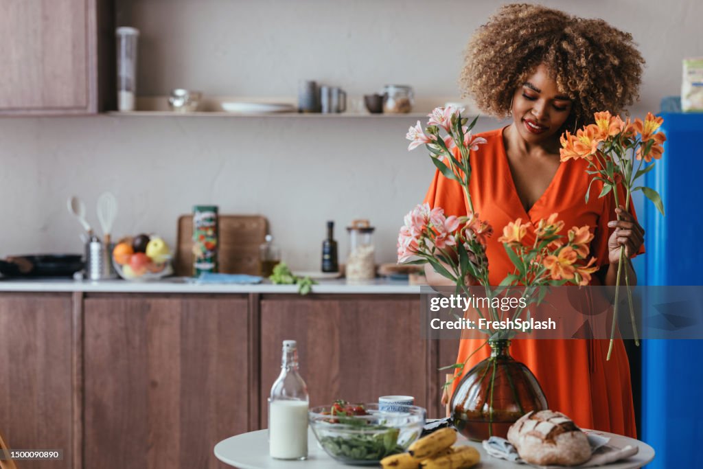 Beautiful African American Woman in an Orange Dress Arranging Pink and Orange Flowers into a Bouquet