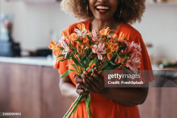 anonyme afroamerikanerin in einem orangefarbenen kleid, die einen blumenstrauß hält - blumenstrauß stock-fotos und bilder